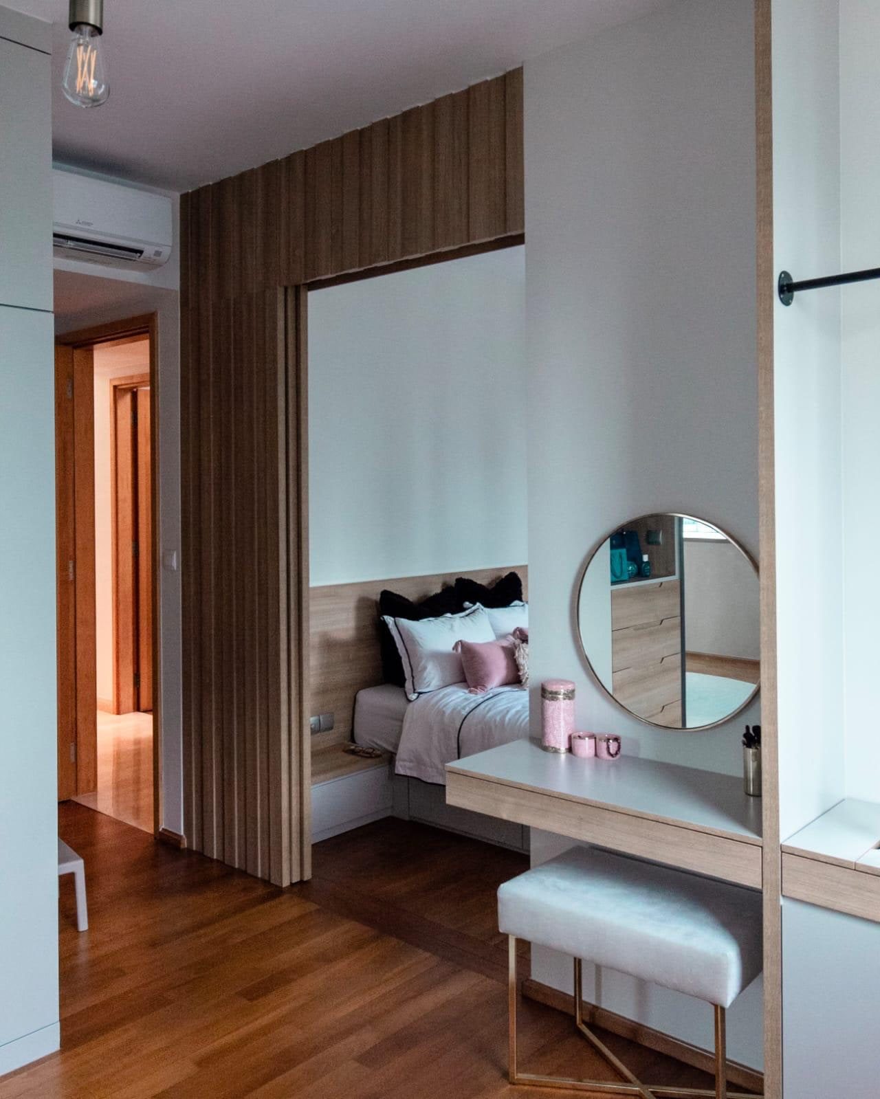 A bedroom threshold in a Newton condominium, with a screen of full-height timber battens slid back to open the bed alcove, and a dressing table with a round mirror and a gold-legged stool beside it.
