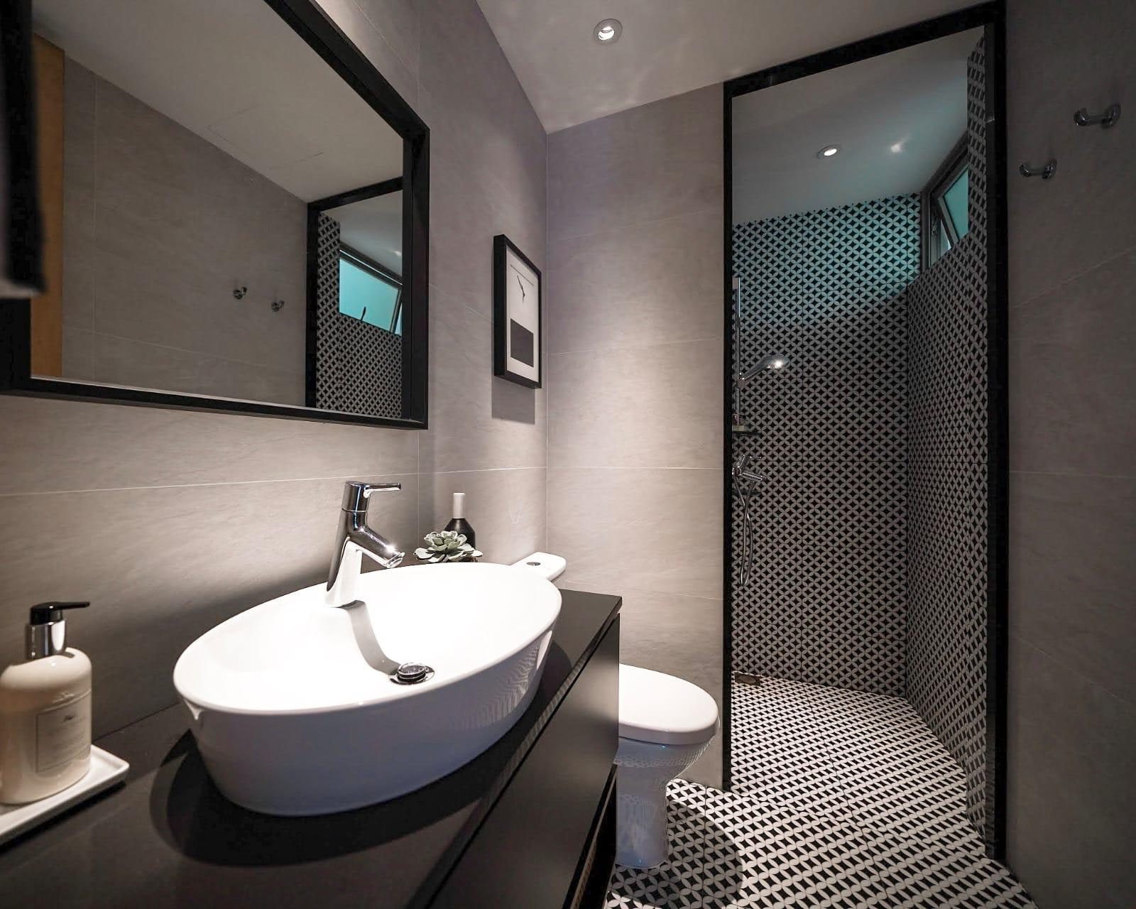 A second bathroom in a Newton condominium in grey large-format tile, with an oval vessel basin under a black-framed mirror and a round black and white mosaic lining the shower.