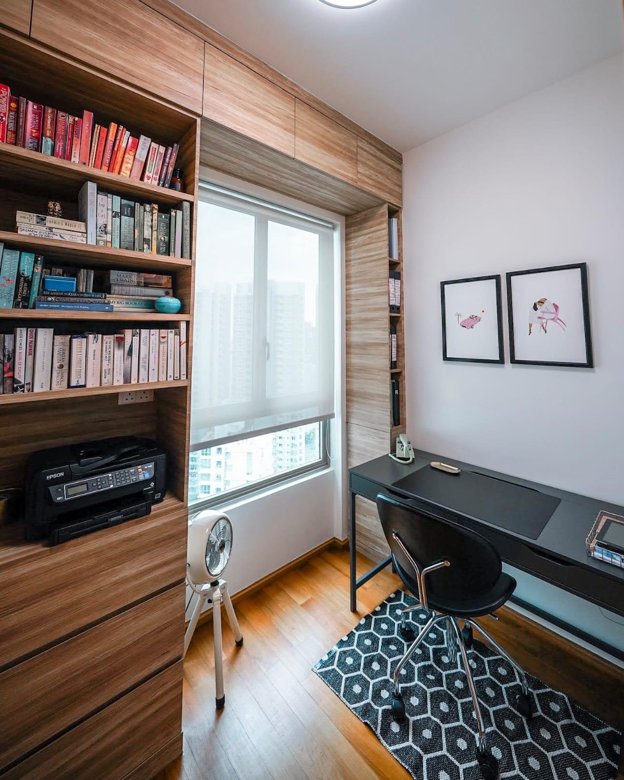 A study in a Newton condominium lined on three sides with timber shelving around the window, holding a full-height run of books above a black desk.