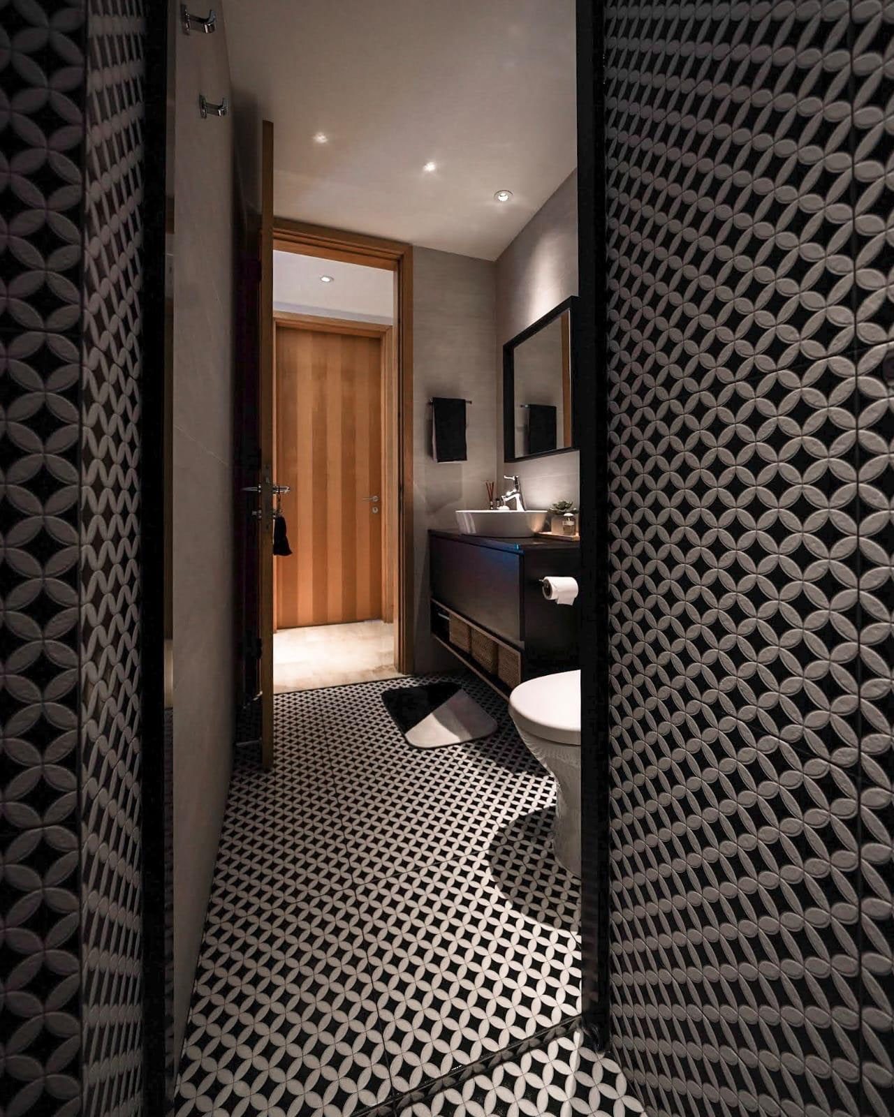 A powder room in a Newton condominium walled in dark relief-patterned tile, with a patterned mosaic floor and a timber door standing open to the hall.