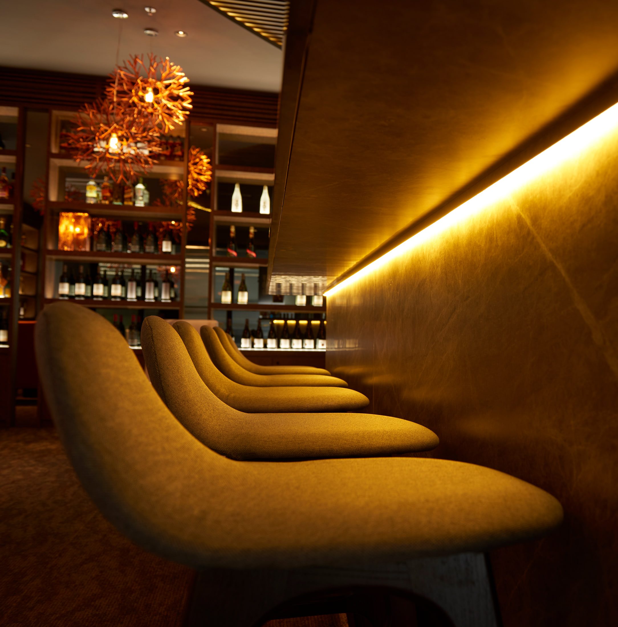A run of curved mustard banquette seats along a brass wall with a recessed light line, wine shelving standing beyond.