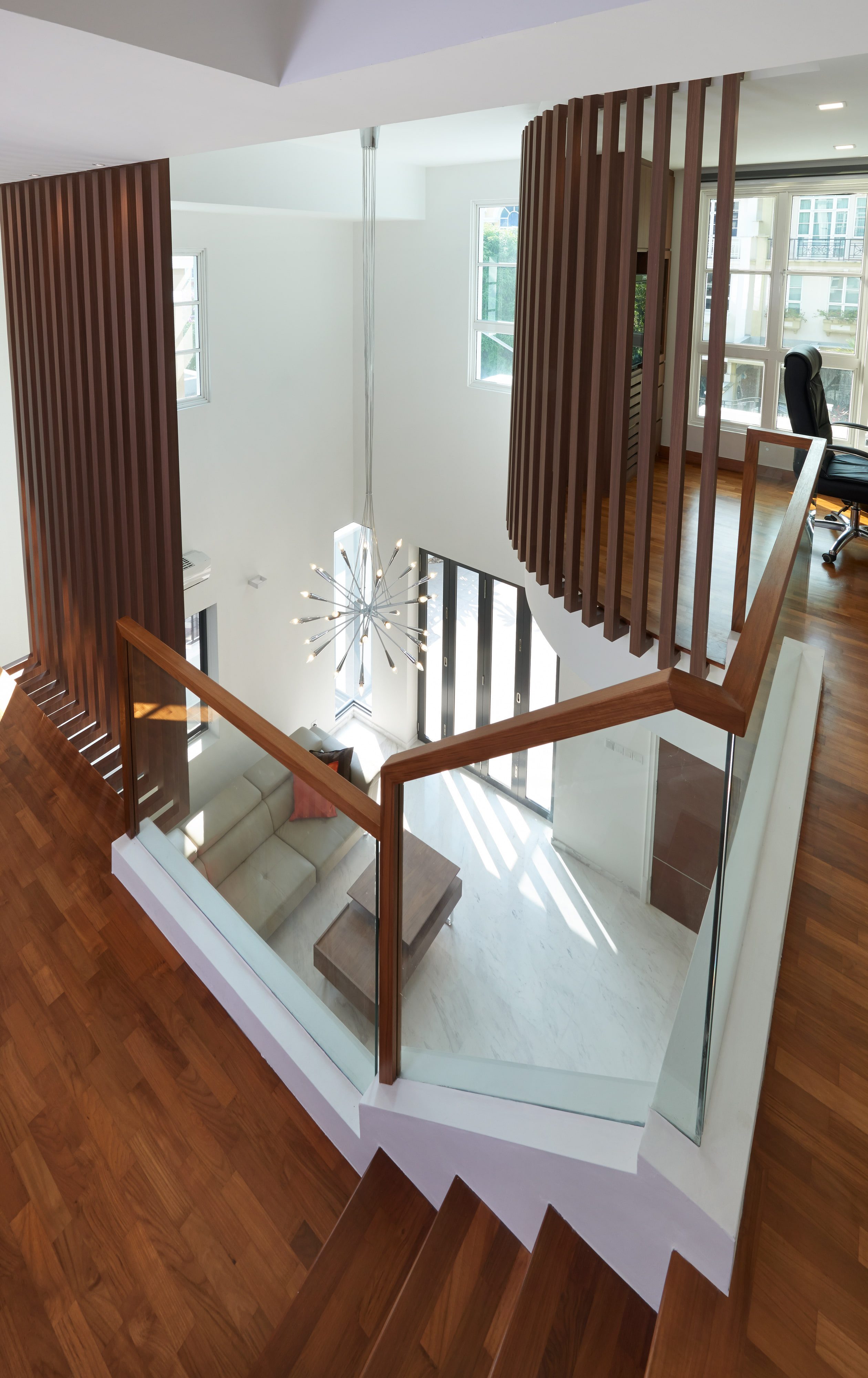 An upper landing behind a glass balustrade, a curved timber slat screen enclosing the stair void and a timber handrail returning down.
