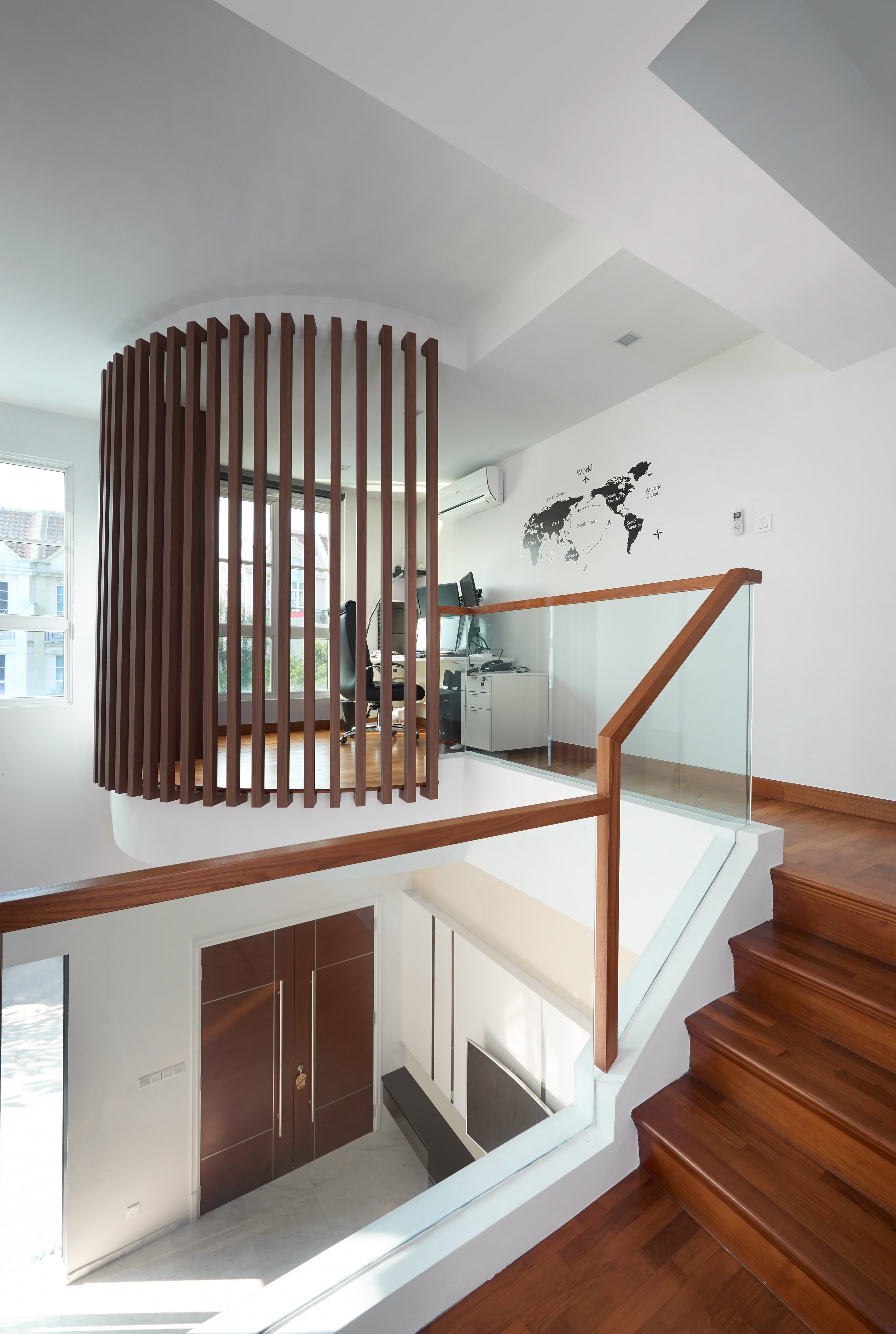 The stair void seen from the landing, a curved drum of timber slats screening it and a map applied to the wall beyond.