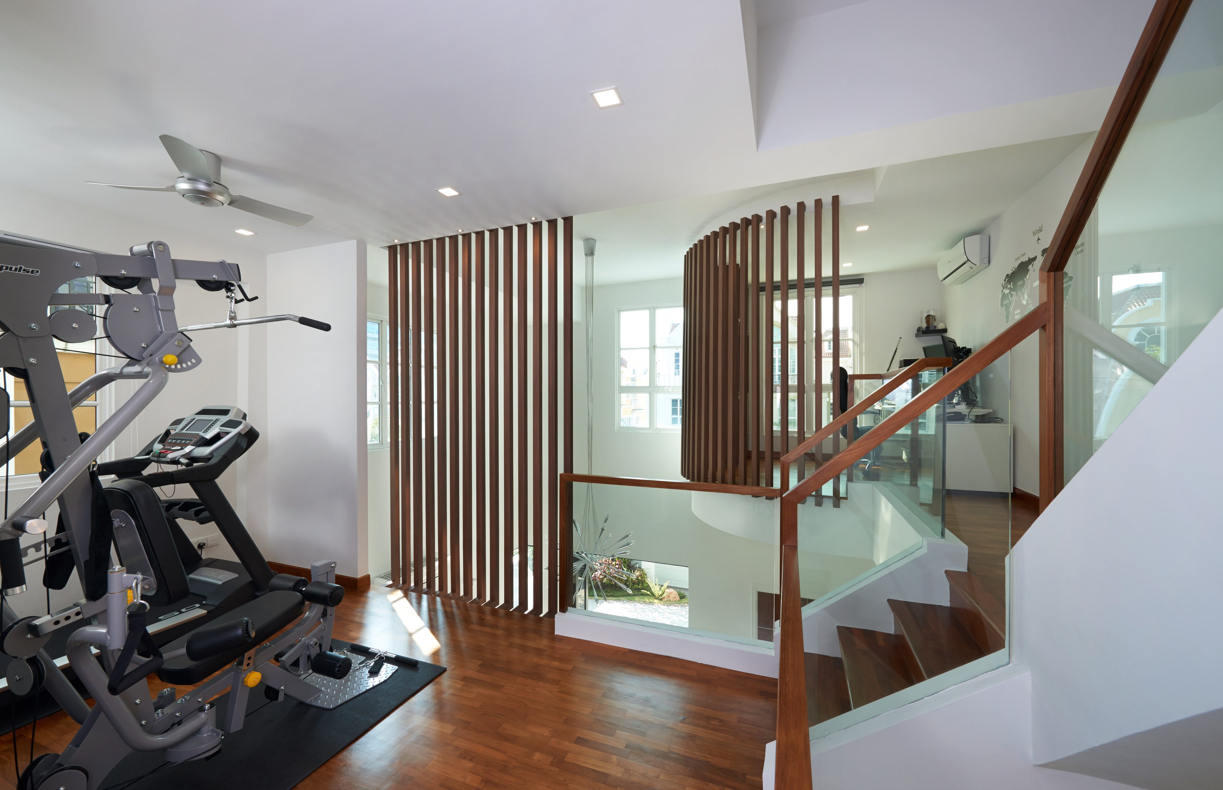 An upper-floor gym with a treadmill and cross trainer on a matted floor, beside the curved timber slat screen at the stair.