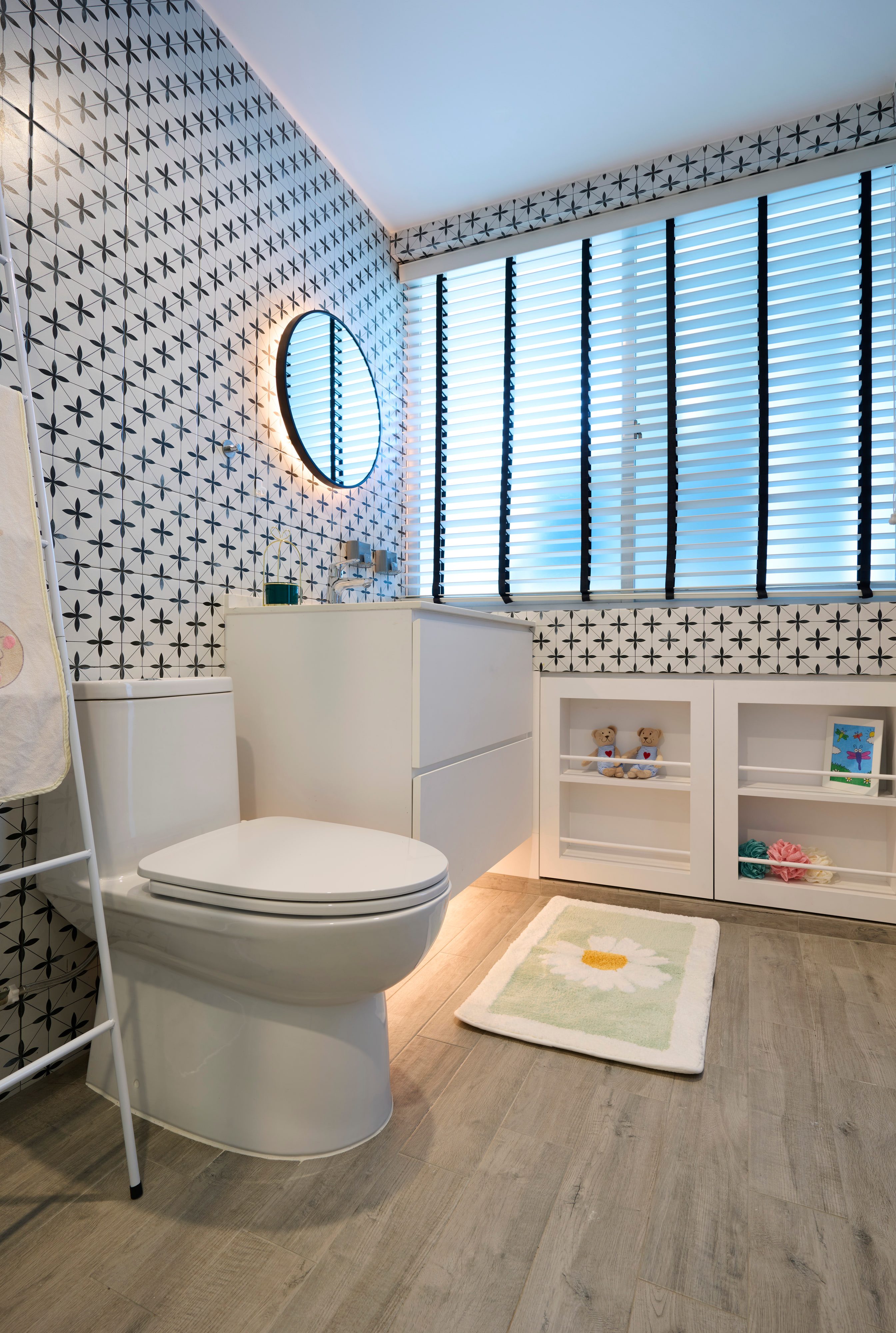 A child's bathroom tiled in a black and white cross pattern, with an oval mirror, a low white storage unit and a soft mat.