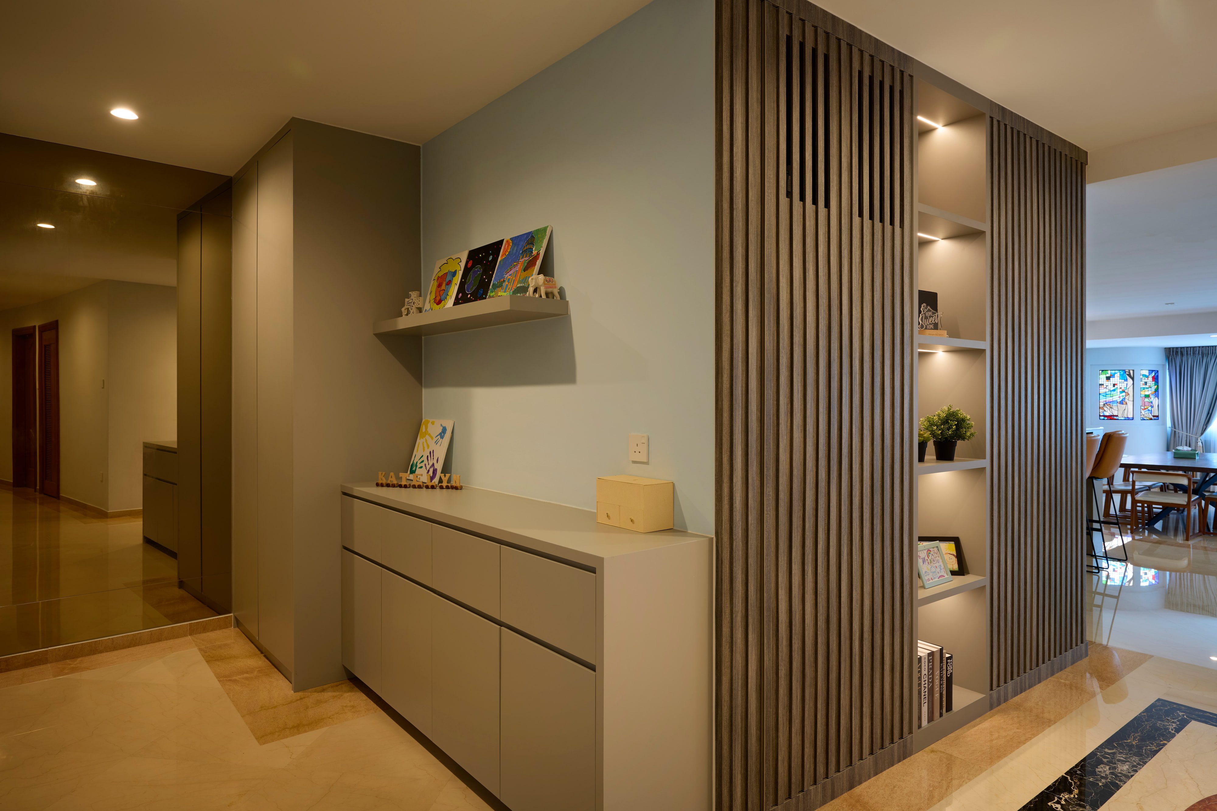 The corridor face of the timber slat screen, with a greige console run, open shelving lit from within and the dining room beyond.