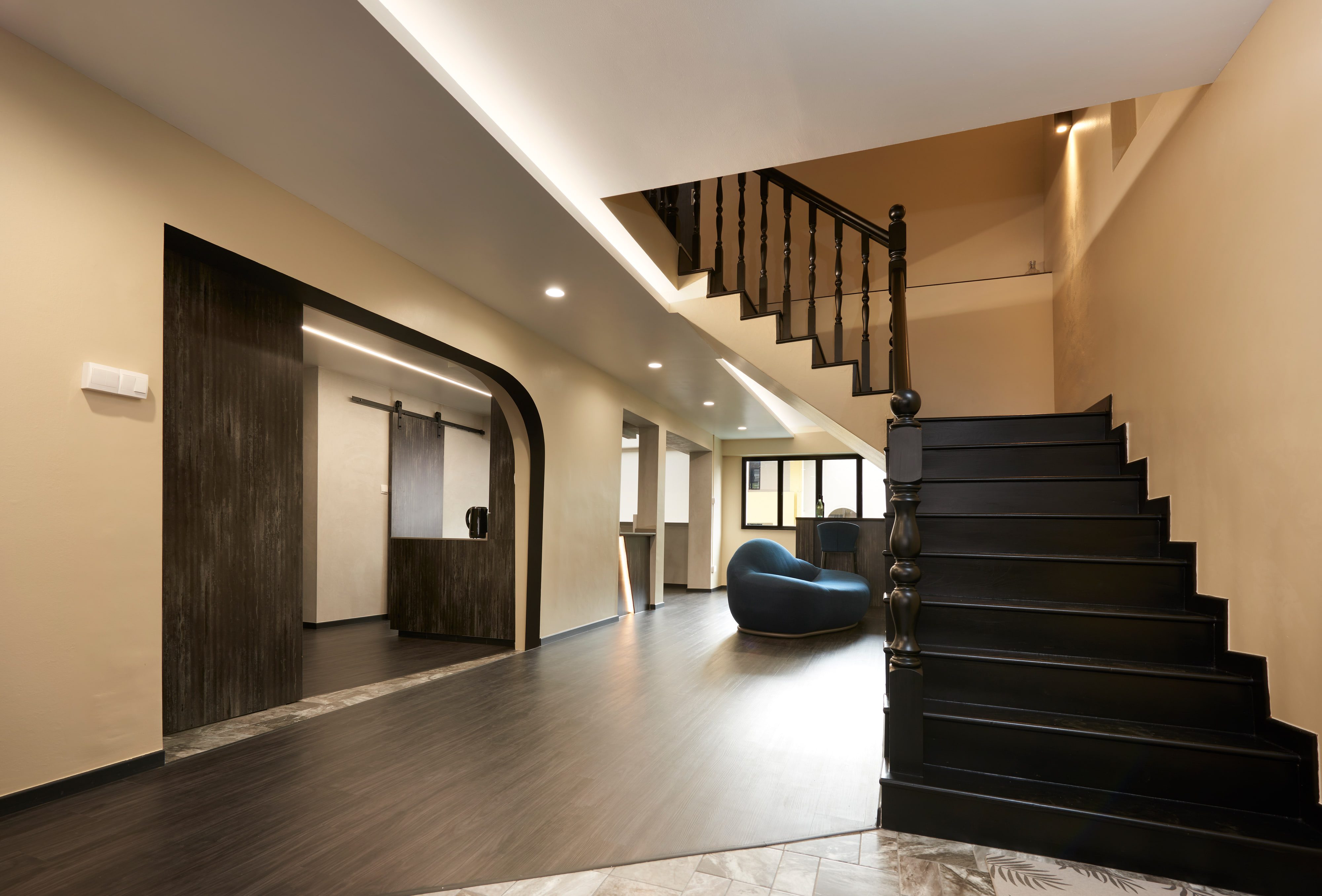 The same hall with the sliding panel pushed clear of the arch, opening the view through to the lit worktop and the barn door on its black track beyond.