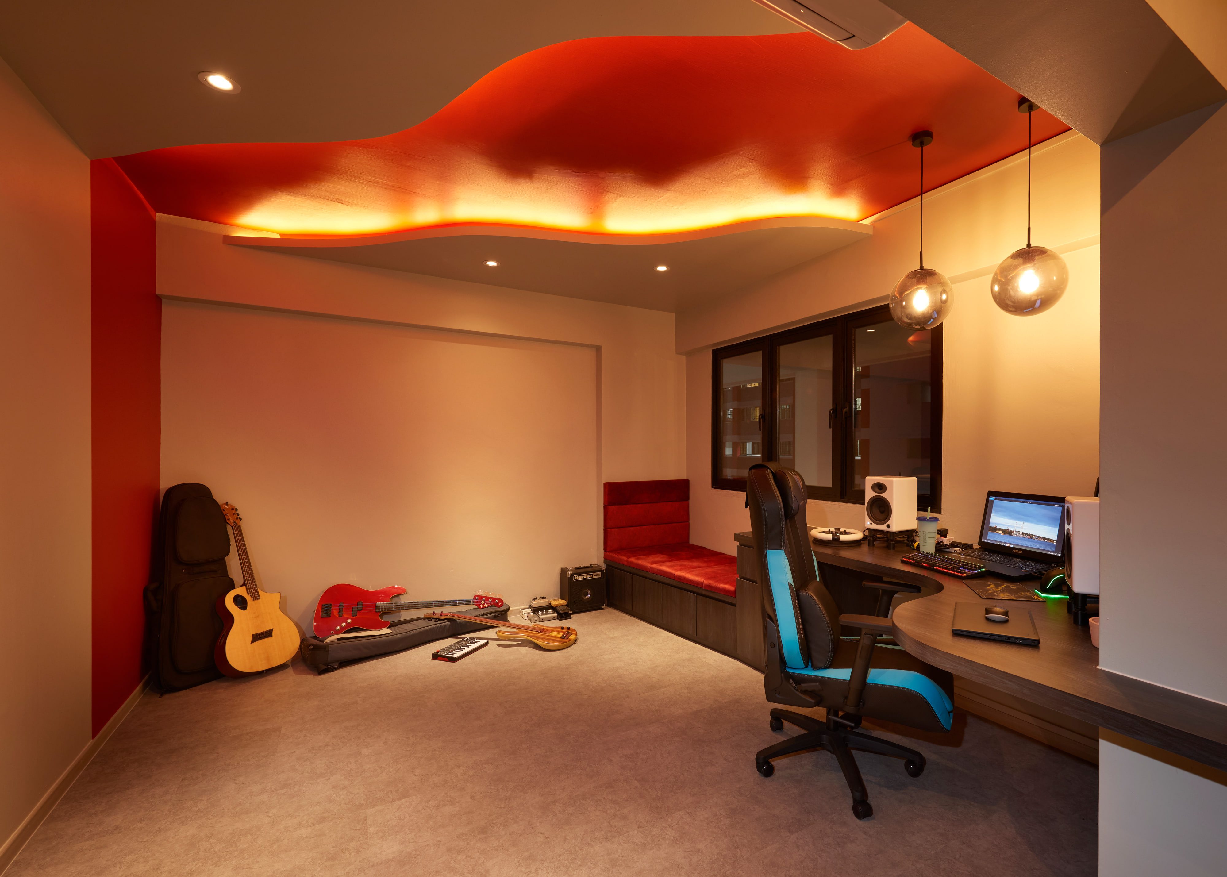 A study and music room with a curved scarlet ceiling raft lit from beneath, a wrap-around desk, a red upholstered window bench and guitars and a small amplifier resting along the wall.
