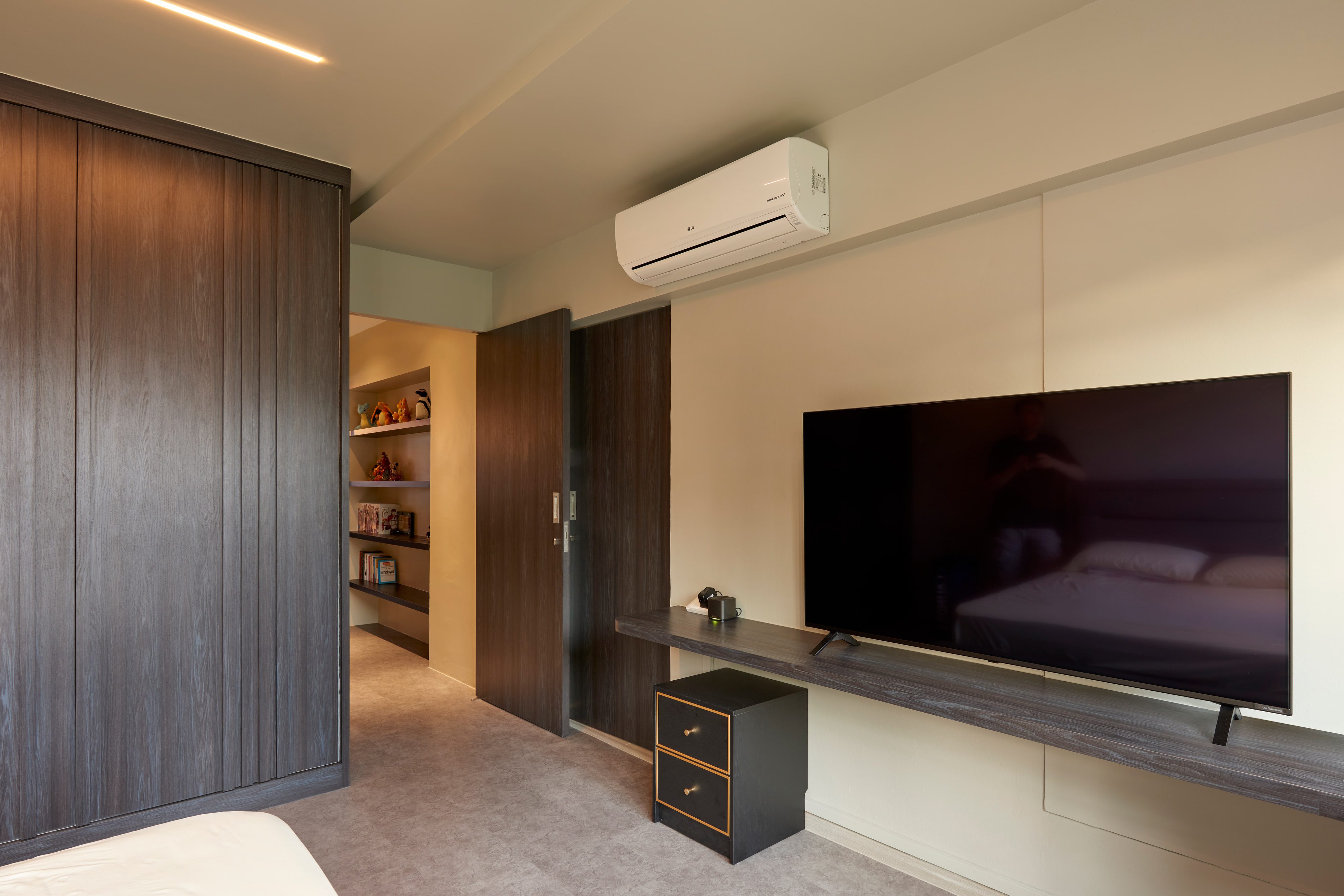 A bedroom with a dark timber wardrobe wall, a television on a slim ledge and a doorway through to the landing beyond.