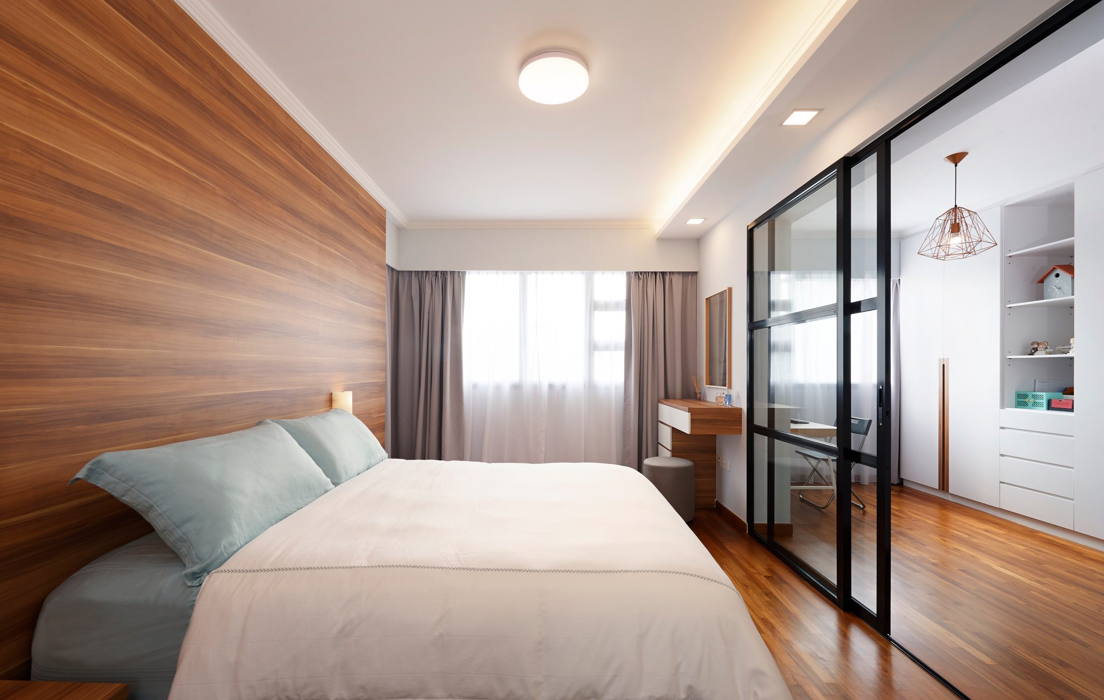 The main bedroom with a full-height timber headboard wall, a cove-lit ceiling and a black-framed glazed sliding screen opening onto a small study beyond.