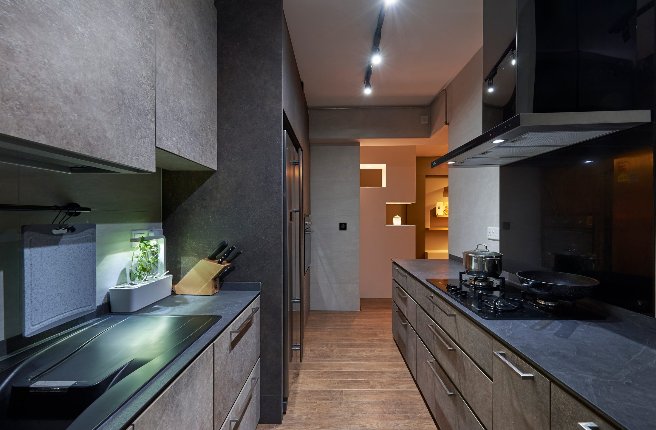 A galley kitchen in stone-effect laminate with a dark grey worktop, a chimney extractor over a gas hob, and a lit niche at the far end of the run.