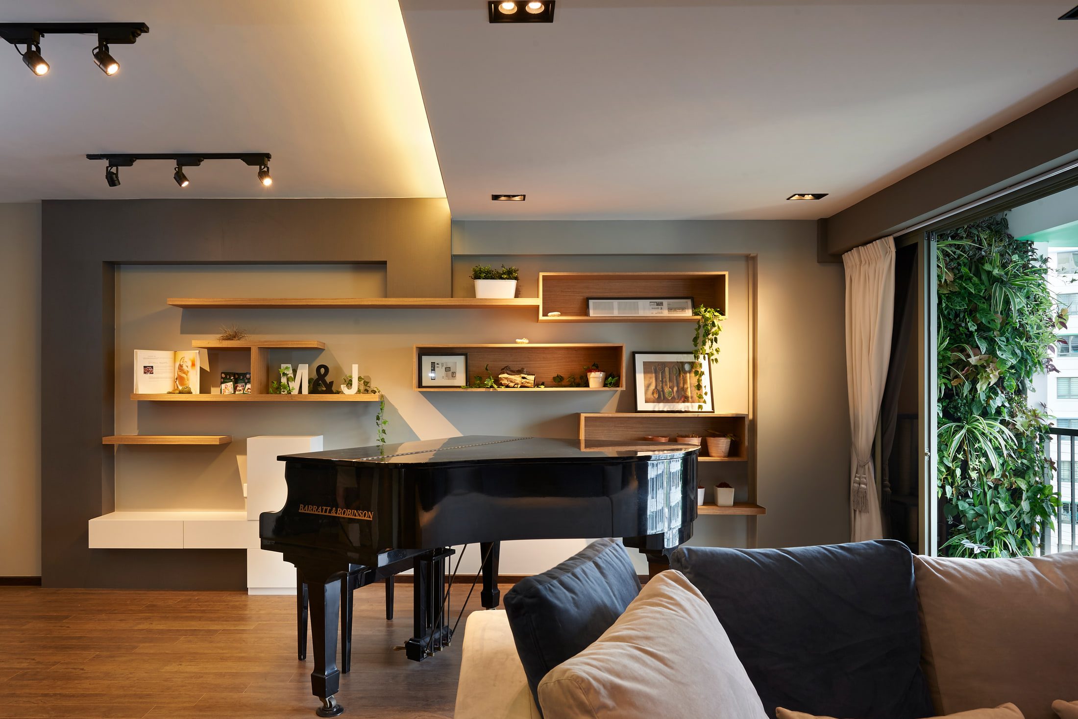 A grand piano seen across a sofa back, framed by a wall of oak shelves and glazed boxes with a planted balcony to the right.
