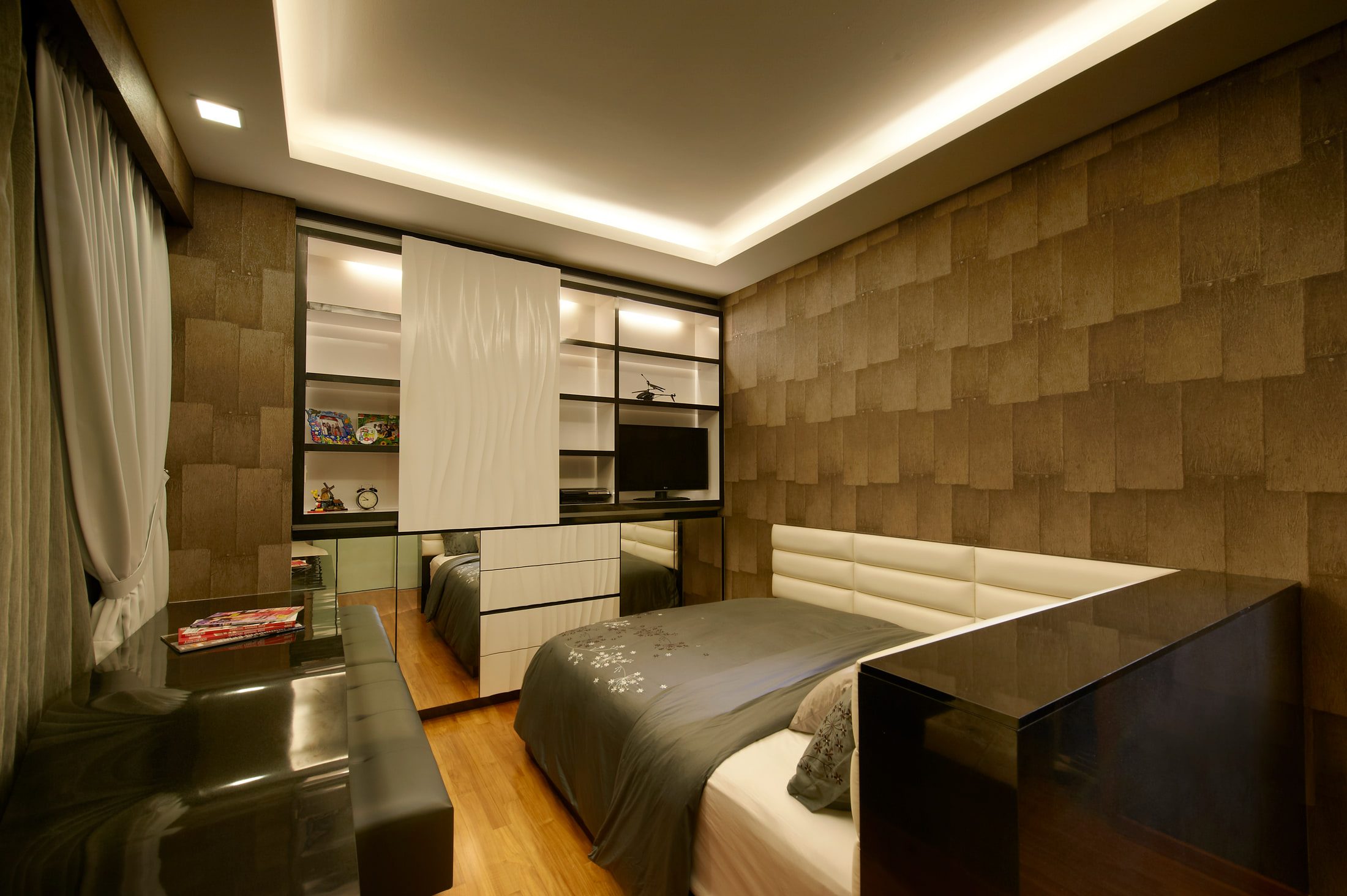 A bedroom lined in textured square-block wallpaper with a lit display and study wall, a white buttoned headboard and a black glass desk running under the window.