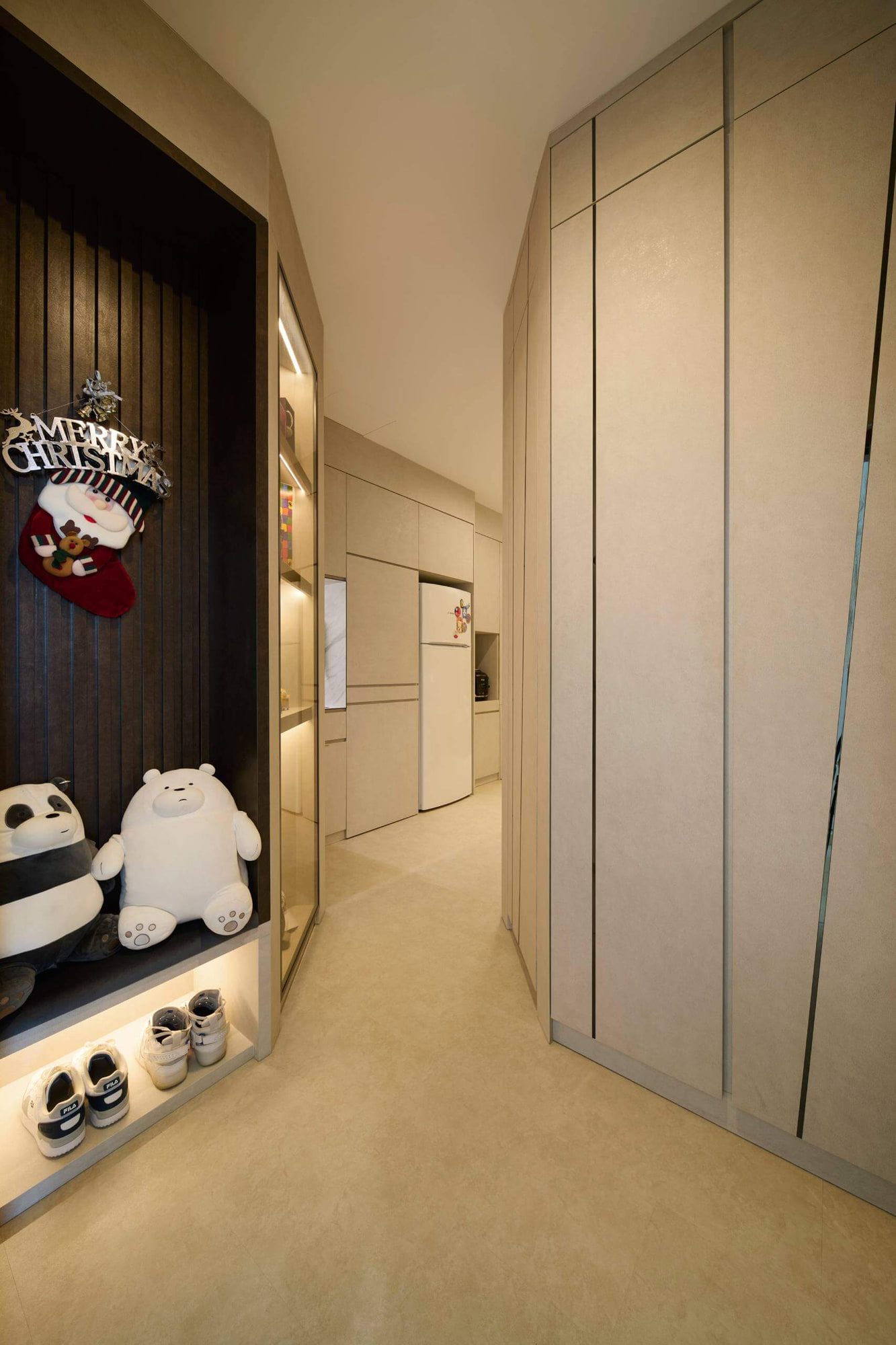 A narrow entry corridor lined floor-to-ceiling in pale stone-effect joinery, with a lit display niche against dark fluted panelling and a kitchen beyond.