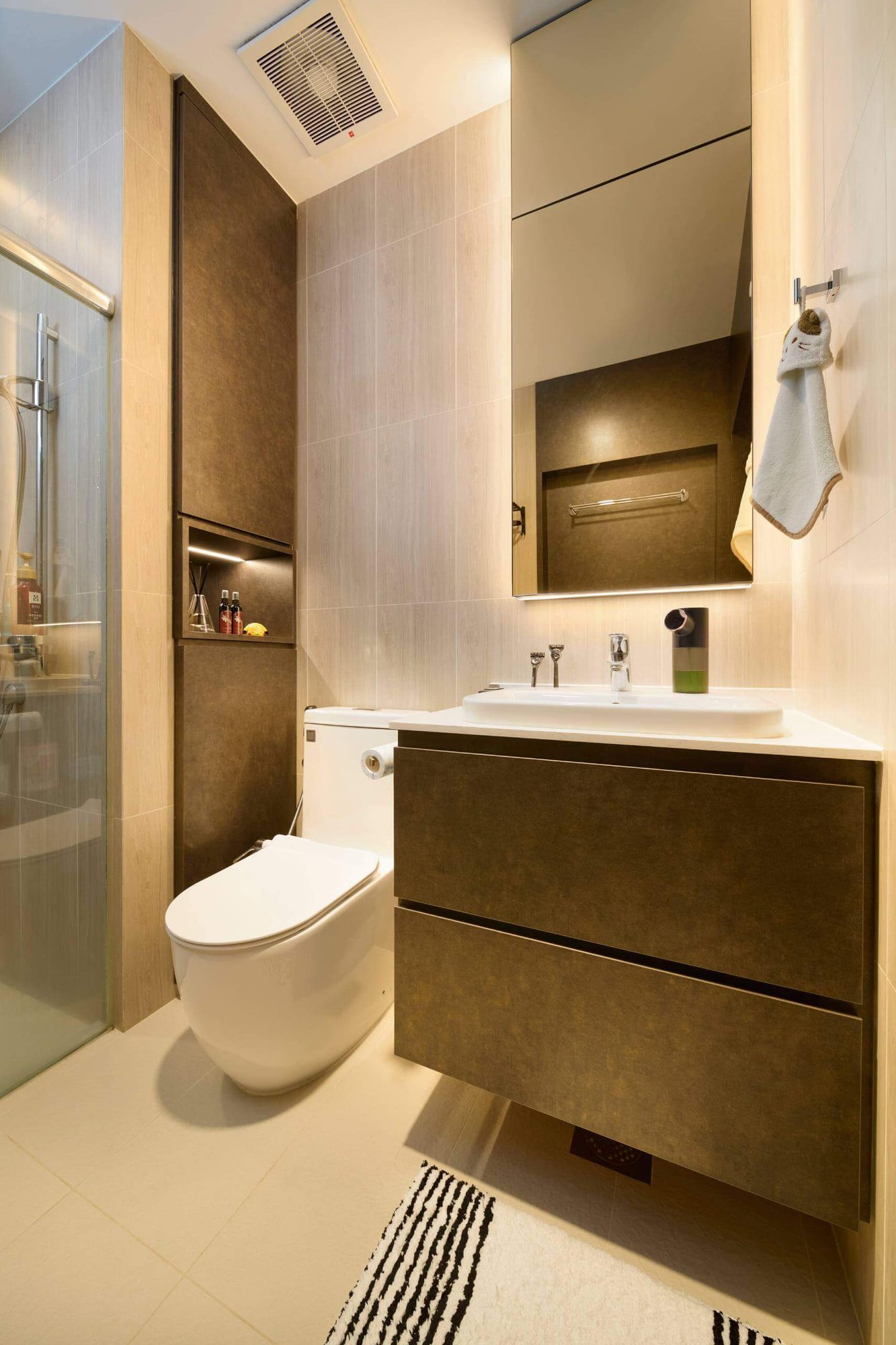 A bathroom with a bronze-fronted wall-hung vanity, a mirrored cabinet above and a wall-hung WC beside a glazed shower.