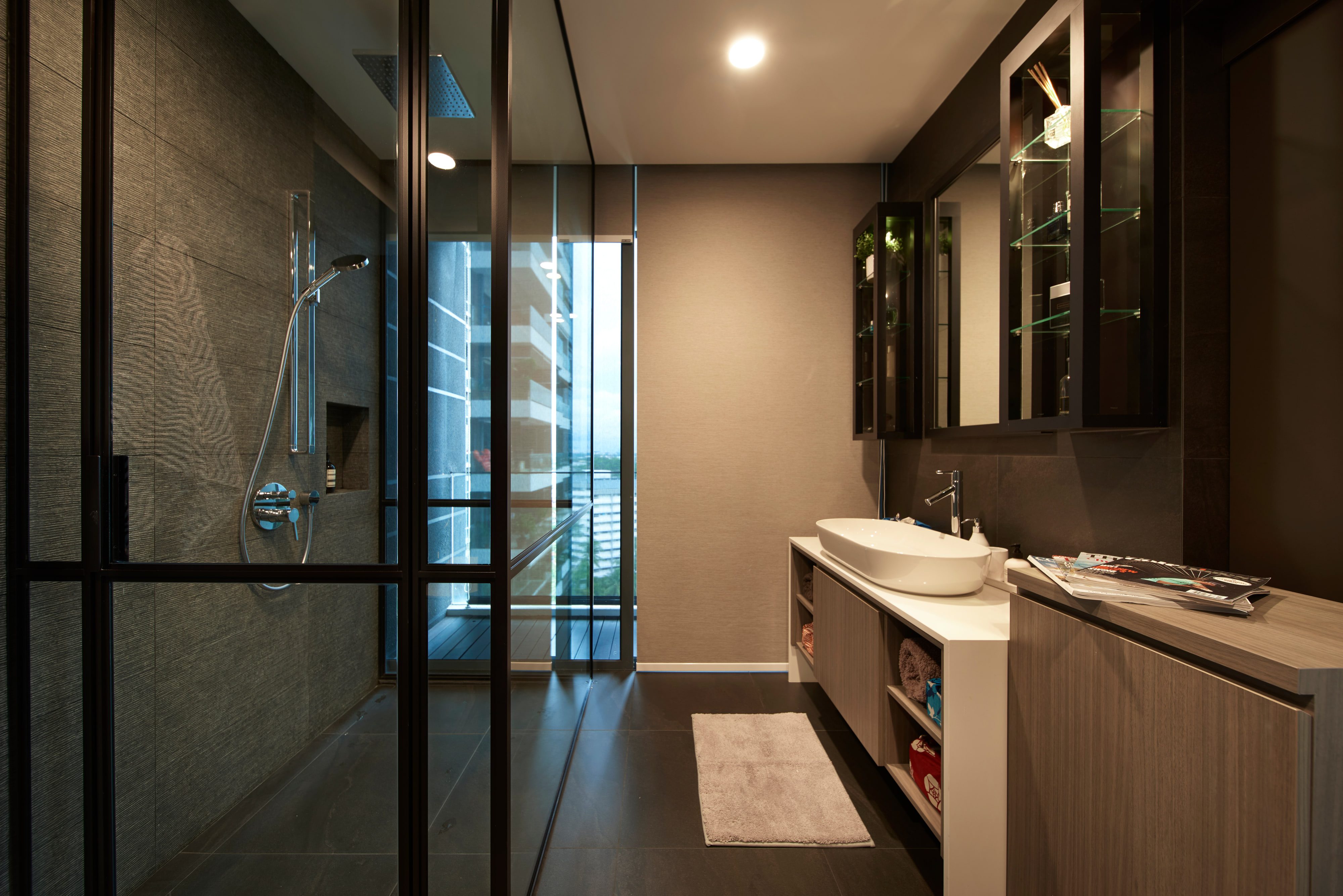 The same bathroom with the balcony door closed, the glass shower screen at left and the vanity's stepped stone top and open towel cubbies at right.