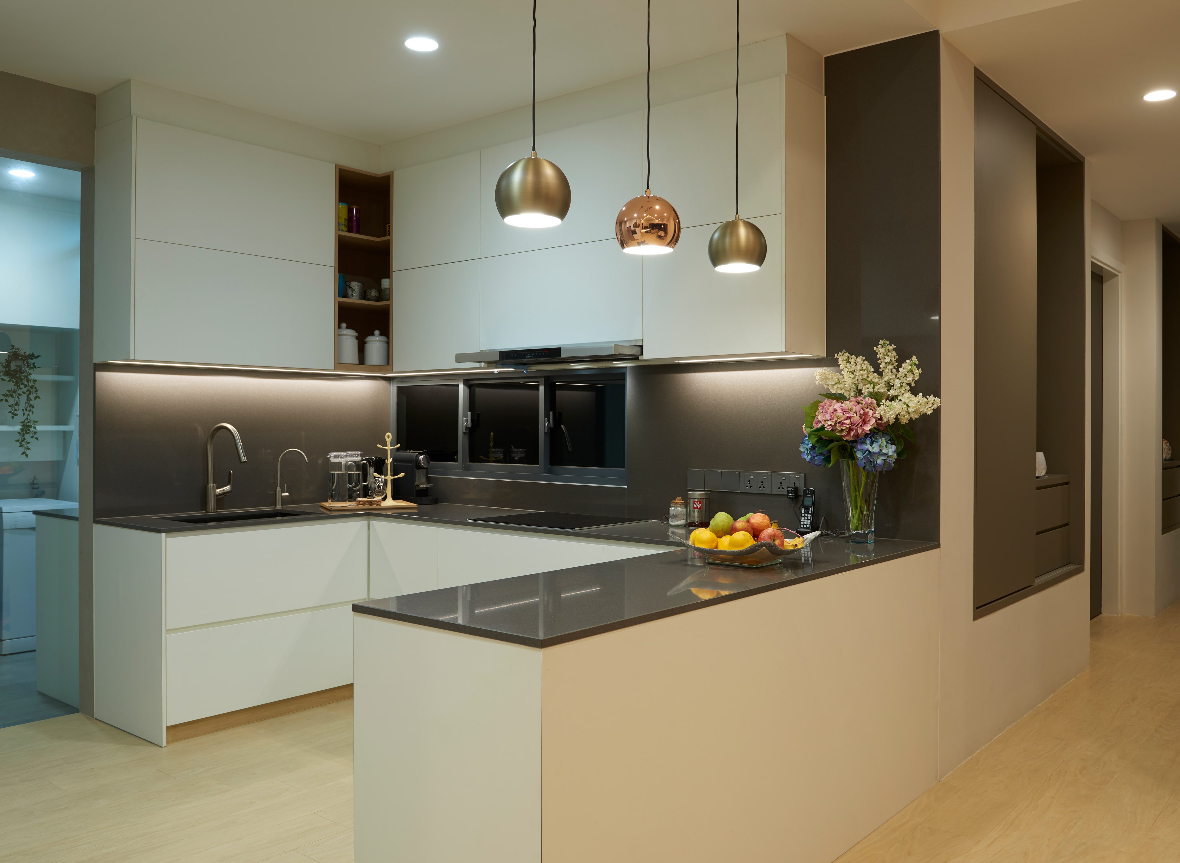 Handleless cream kitchen cabinets under a graphite quartz worktop and matching glass splashback, with brass and copper globe pendants over the peninsula.