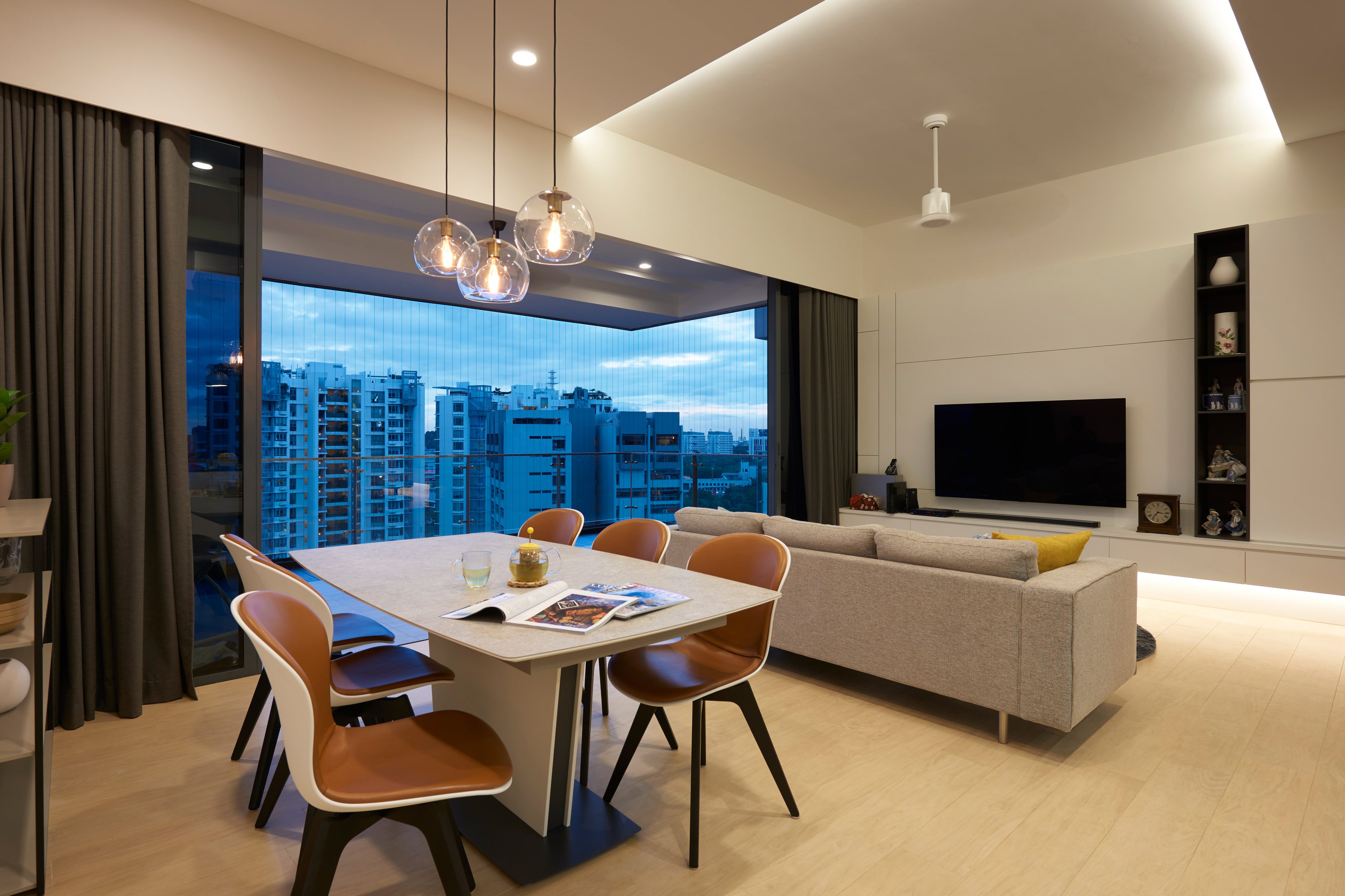 An open living and dining room with a flush white media wall, two black display niches, an oatmeal sofa and tan leather chairs beneath glass globe pendants.