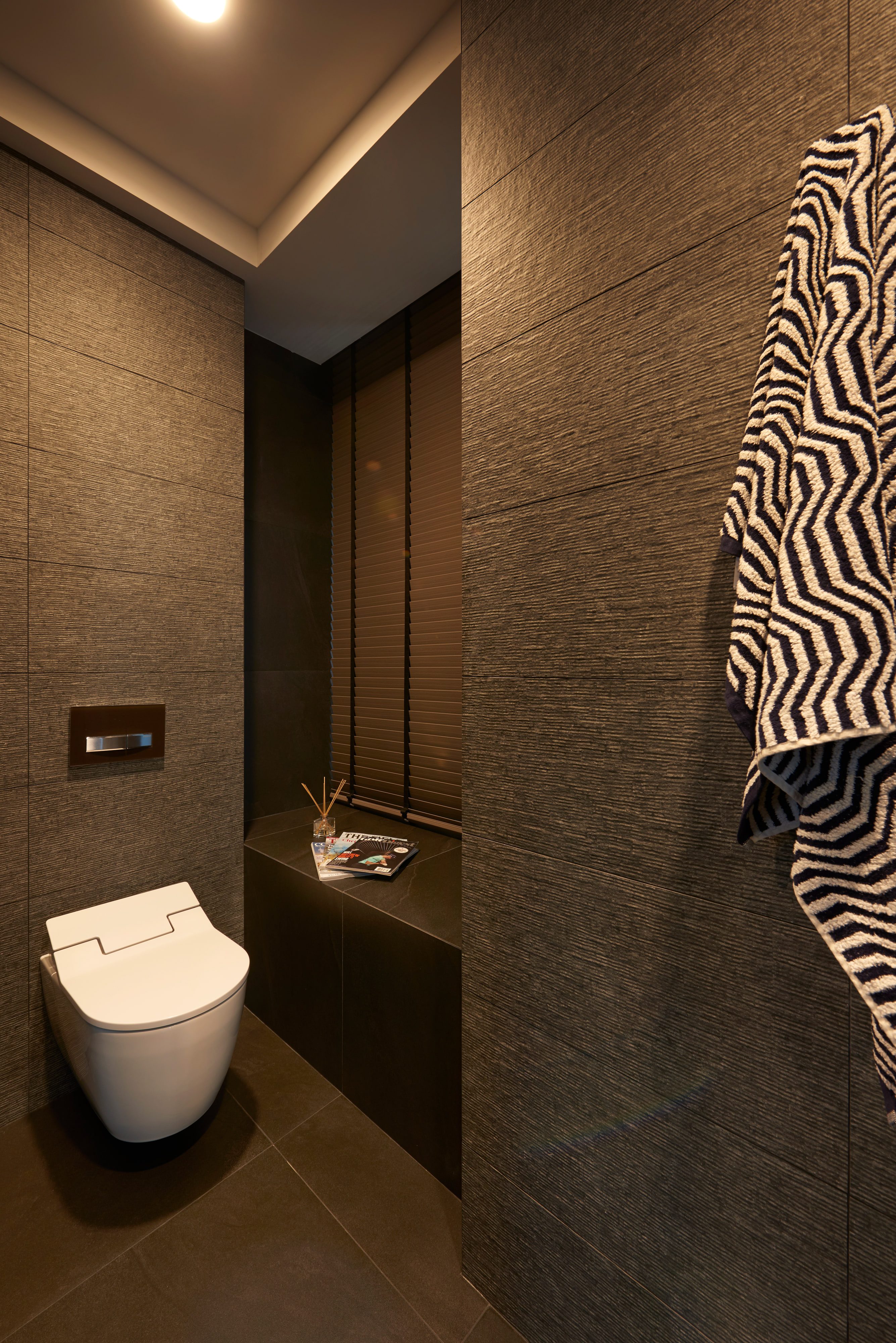 A bathroom lined in dark riven stone, with a wall-hung WC, a concealed cistern panel and a patterned towel on a rail.